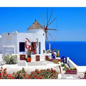 Canvastavla 70x100 cm - Pittoresk vy av en vitkalkad byggnad med en traditionell vindmölla och färgglada blommor i Santorini - Inredning & dekor Utförsäljning