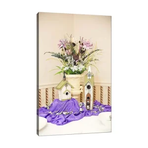 Canvastavla 70x100 cm - Vacker blomsterarrangemang i en kruka med två fågelhus på en lila duk - Inredning & dekor Kampanj