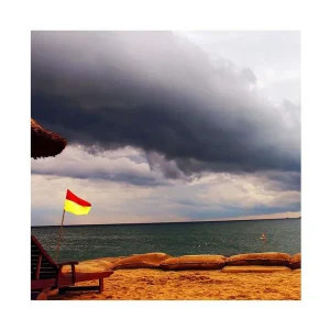 Köp nu Canvastavla 45x45 cm - Flagga med röd och gul färg vid en strand med mörka moln i bakgrunden Mörkgrå / Röd / Gul - Inredning