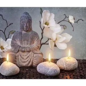 Canvastavla 70x100 cm - Sittande Buddha omgiven av blommor och stenar med tända ljus - Inredning & dekor Rabatter