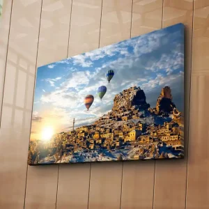Canvastavla 70x45 cm - Färgglada luftballonger sväva över en pittoresk bergsby vid soluppgången Guld / Blå / Orange - Inredning Premium
